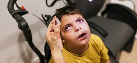 a boy with neurodevelopmental disorders looking upward while a clinician holds a small object near his eyes during an eye-movement exam
